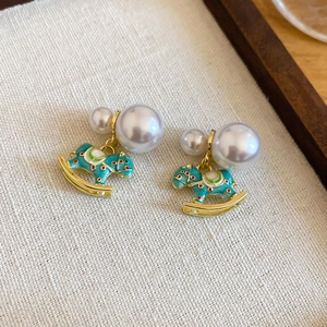 Macro detail of enamel rocking horse pearl earrings with golden trim on fabric base