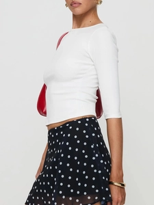 Side view of white slim fit long sleeve top paired with black polka dot midi skirt