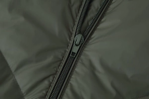 Detailed macro view of the smooth resin zipper and quilted fabric on a green cotton coat
