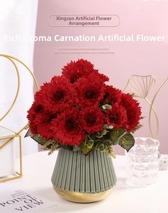 Deep red artificial carnations with green leaves in a ribbed ceramic vase with gold base trim
