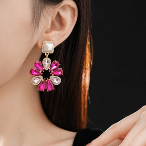 Dettaglio di orecchino a fiore con cristalli rosso rosa e perla bianca su una modella