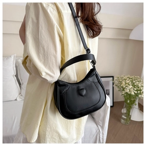 Model wearing a black crescent shoulder bag with heart relief in a cozy home setting