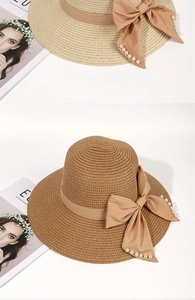 Detail of woven straw sun hat featuring a large ribbon bow and elegant pearl accents