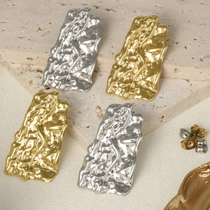 Macro detail of textured gold and silver 304 stainless steel earrings on beige travertine