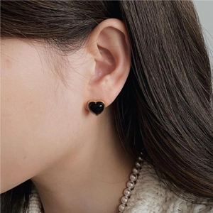 Elegant close-up of a black heart earring with gold border worn by a model