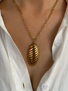 Detail of a large gold oval cutout pendant on a paperclip chain worn over a white shirt