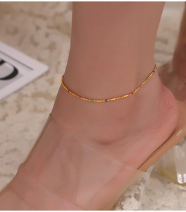 Close-up of golden titanium steel anklet with colorful beads on a lace background