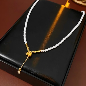 Macro view of gold gourd pendant with pearls and long tassel on black display box