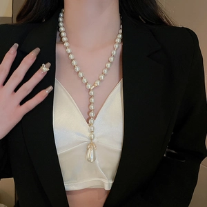 Model wearing a French-style Y-shaped golden pearl necklace with leaf detail over a black suit