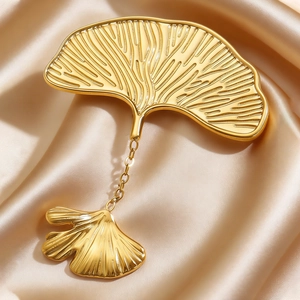 Detail of golden ginkgo leaf brooch with vein texture on champagne silk fabric