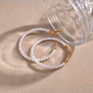 Close-up of elegant gold C-shaped hoop earrings with white pearls on a sandy background