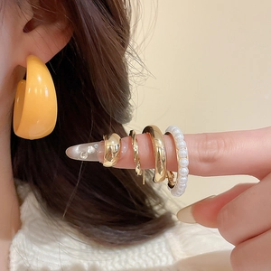 Detail of yellow acrylic hoop earring and layered gold rings with a pearl band