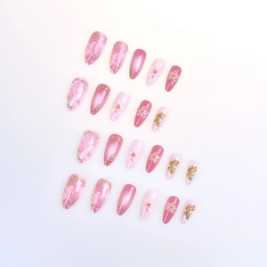 Close-up of pink almond press-on nails featuring 3D flowers, pearls and golden marble accents