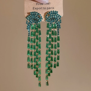 Détail de boucles d'oreilles franges vert émeraude avec monture dorée et pompons