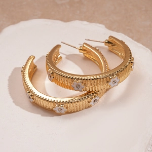 Detail of gold C-shape hoop earrings with white enamel flowers and rhinestone accents