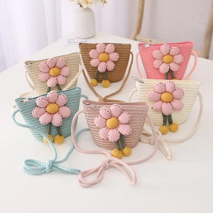 Detail of children's straw crossbody bags with 3D floral accents and fuzzy pom-poms