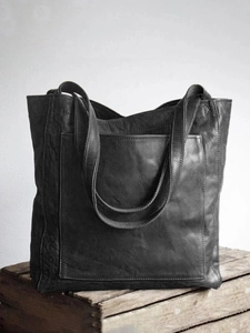 Gros plan d'un cabas vintage en cuir noir avec poche frontale posé sur une caisse en bois