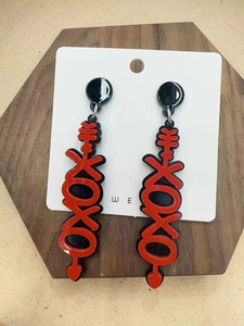 Close-up of red acrylic XOXO drop earrings with heart charms on a wooden display base