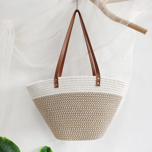Two-tone woven cotton tote bag with leather handles hanging on a branch for summer beach vacation