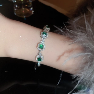 Macro detail of French style emerald bracelet with diamonds worn on wrist with feathers