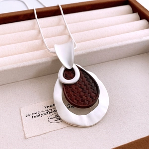 Close-up of matte silver hollow pendant with dark brown woven wood inlay and sleek snake chain
