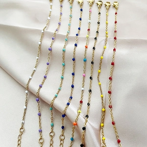 Minimalist gold link bracelets with colorful enamel beads on a soft pink satin background