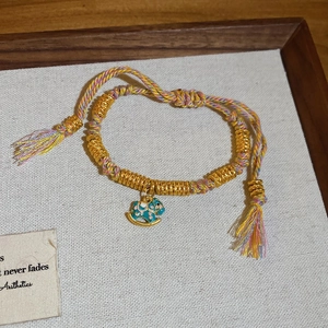 Detail of colorful woven rope bracelet with gold beads and enamel rocking horse charm