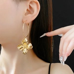 Close-up of golden metallic flower drop earrings featuring a large hoop and textured petal
