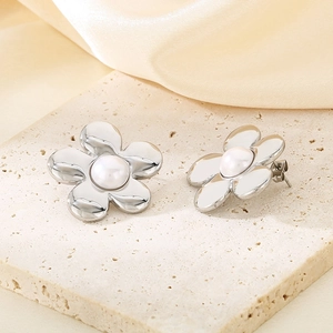 Detail shot of silver flower earrings with white pearl centers on a beige stone surface