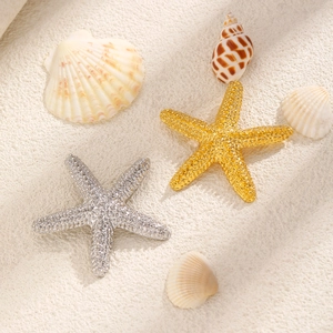 Starfish brooches in gold and silver finish on beach sand background with seashells