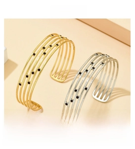 Détail de bracelets ouverts multicouches dorés et argentés avec points en émail noir