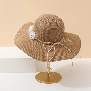 Détail d'un chapeau de soleil tressé beige avec pompons fleurs blancs et un nœud en corde