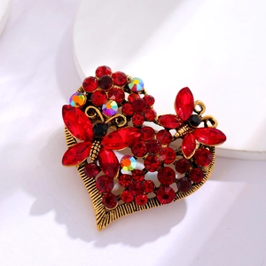 Detailansicht der goldenen Herzbrosche im Vintage-Stil mit roten Strasssteinen und Schmetterling