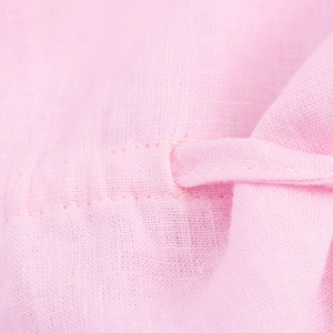 Close-up of pink linen fabric texture showing the drawstring eyelet detail on the shirt
