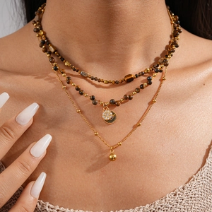 Detail of layered 18k gold-plated necklaces with tiger eye beads and pavé round pendants