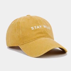 Detail of white STAY WILD embroidery on washed mustard yellow cotton baseball cap