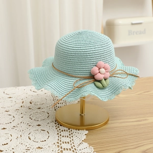 Detail view of light blue straw hat with 3D pink flowers and a wavy brim on a gold stand
