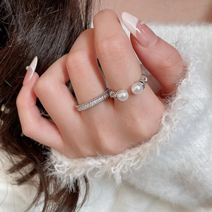 Detail of silver double pearl ring and zircon band worn on hand against white knit fabric