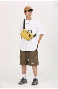 Detailed view of yellow crossbody chest bag featuring black zippers and adjustable strap