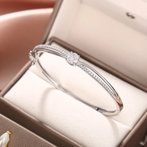Detail of silver crossover bangle with central round zircon in a premium jewelry box