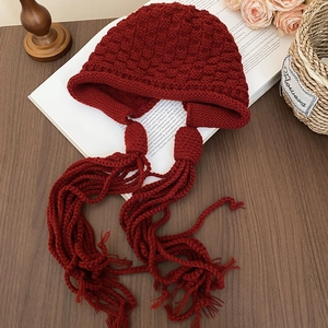 Close-up of burgundy knit beanie with thick pineapple stitch texture and long tassels