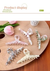 Five acetate claw clips with marble texture patterns on a wooden palette with flowers