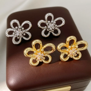 Detailed close-up of hollow flower stud earrings with zircon inlay in gold and silver