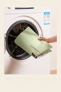 Close-up of a large green quilt storage bag being placed into a washing machine drum
