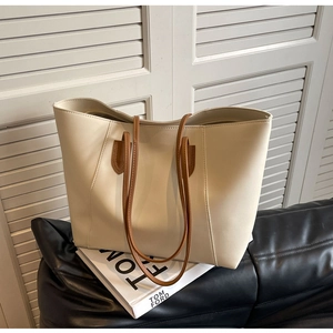 Minimalist cream white tote bag with brown straps on a black leather sofa detail view