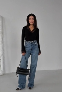 Detail of a black lace long sleeve top paired with blue wide-leg jeans and leather bag