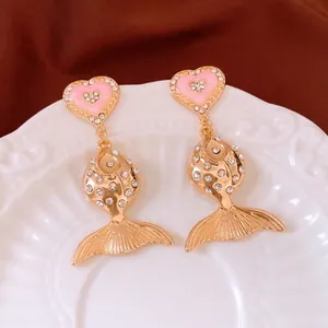 Vintage gold fish earrings with heart shape and sparkling rhinestones on a white plate