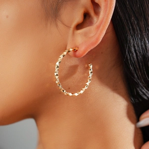 Close-up of geometric twisted C-shape golden earrings with multifaceted texture on a model