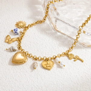 Détail de collier doré avec breloques cœur, papillon et perle sur un fond blanc texturé