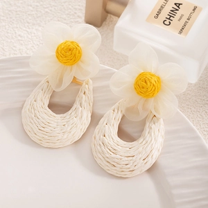 Detail shot of handwoven raffia and mesh flower earrings on a textured white plate